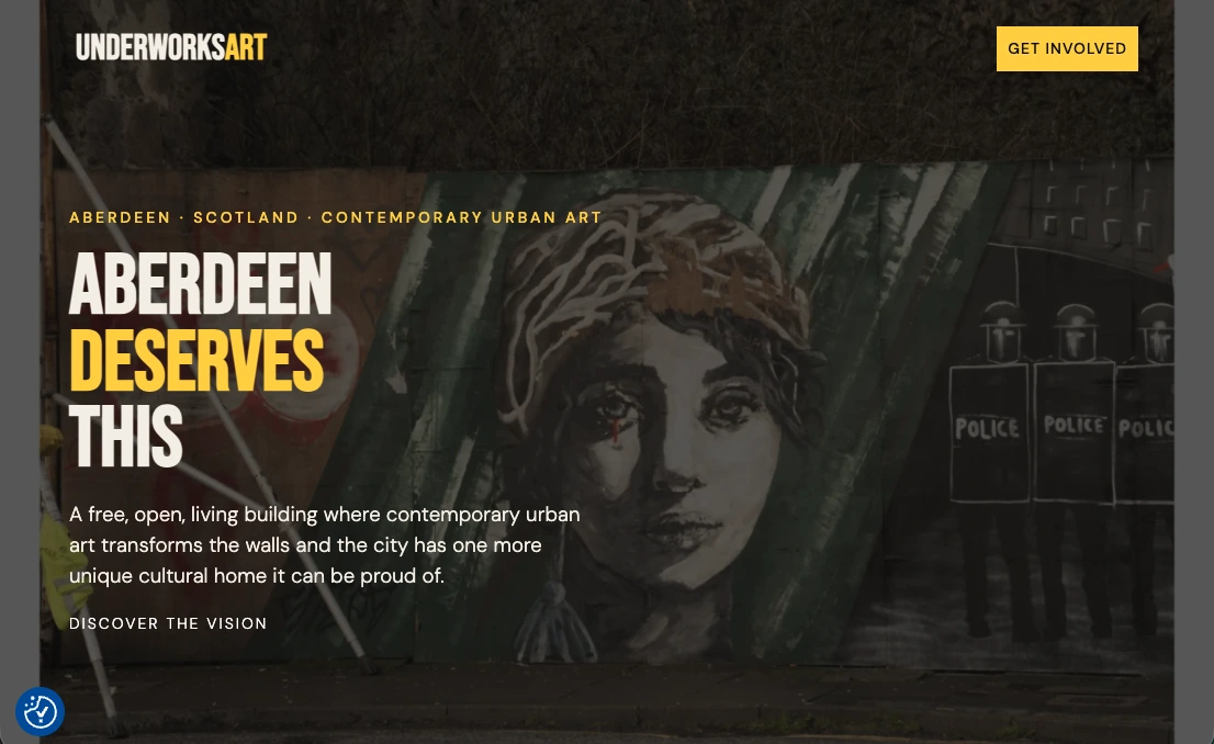 A screenshot of the UnderWorks Art website homepage. The background shows a mural of a crying woman's face on a wooden hoarding. Large white and yellow text reads 'ABERDEEN DESERVES THIS'.